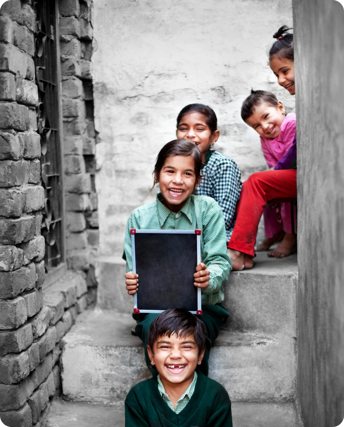 Children smiling on stone steps with chalkboard